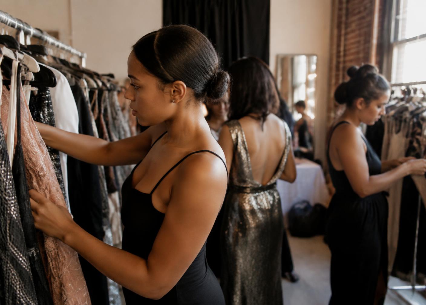 Women preparing outfits on a clothing rail backstage at the fashion showcase